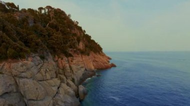 Denizin ve üzerinde ağaçlar olan kayalık sahillerin olduğu güzel bir manzara..