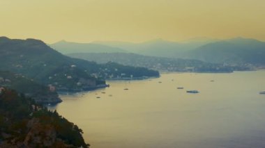 Önünde teknelerin, arka planda dağların, ormanların ve evlerin bulunduğu bir deniz manzarası. 4K