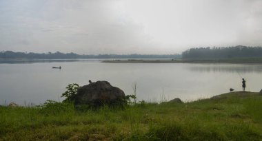 Rezervuar Karangkates Malang Endonezya 'nın önü. Dağlar arasında, gökyüzü sisli. Önünde bir taş ve çayırlar var.