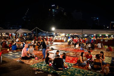 Phnom Penh, Cambodia - January 26 2025 : People eating food outdoor while sitting on the carpets 