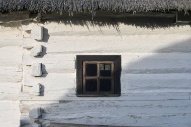 Wall with a window of traditional slavic house, made of wood and roof covered with straw. 