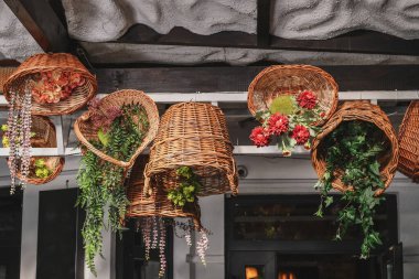 Tavandan sarkan bitkiler ve çiçeklerle dolu sepetler, açık kafenin girişini süsleyin. Seçici odak. 