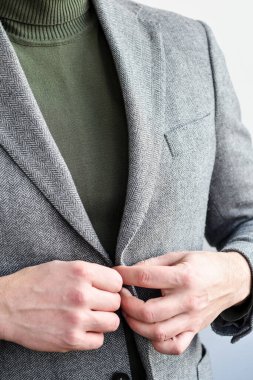 İşadamı gri tüvit ceketin üzerine koyu yeşil kazak takıyor, elleri yakın plan..