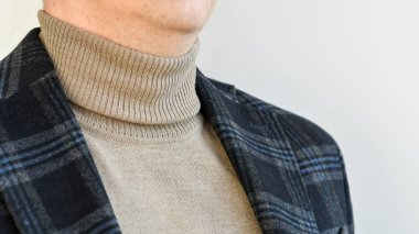 Erkeklerin üstündekileri yakın plan, koyu gri ceket ve bej kazak. Seçici odak.