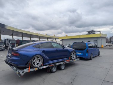 Bulutlu gökyüzünün altındaki benzin istasyonundaki römorkta AUDI A7 spor arabası ayarlandı