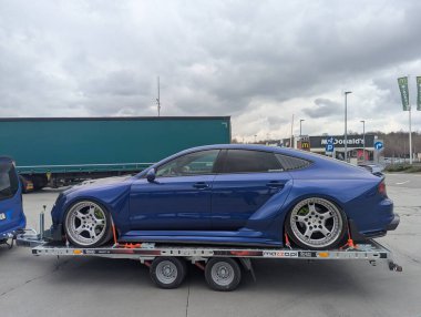 Bulutlu gökyüzünün altındaki benzin istasyonundaki römorkta AUDI A7 spor arabası ayarlandı