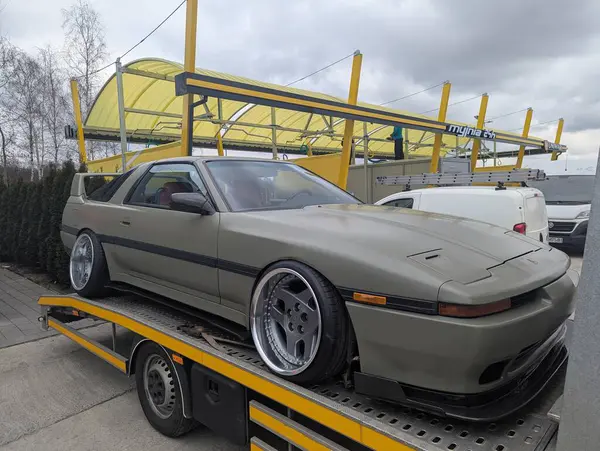 Modifiye edilmiş Toyota Supra Mark III bir benzin istasyonundaki çekici kamyonunda. Özel jantları ve geniş gövdesi olan klasik Japon spor arabası..