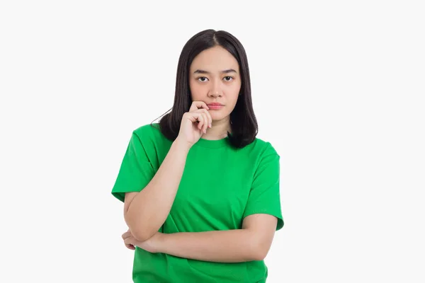 Genç Asyalı kadın yeşil tişört giyerek beyaz arka planda tek başına dikilirken ve düşünürken elini çenesinde tutuyor.