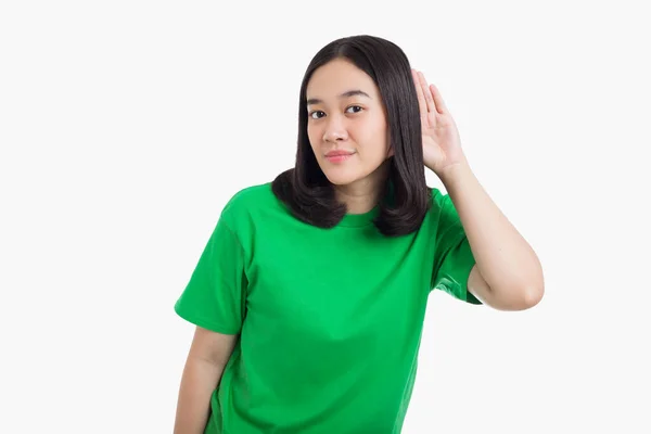 Genç Asyalı bir kadın elini kulağının üzerine koyar. Ya da yeşil tişörtlü bir şey giyer ve beyaz arka planda durur.