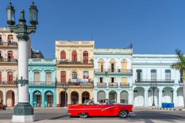 HAVANA, CUBA - 12 Haziran 2022: Eski Havana, Küba 'daki renkli binaların yanından geçen klasik bir üstü açık kırmızı Amerikan arabası.