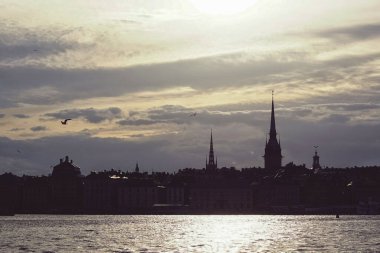 Silhouette of buildings by river against cloudy sky during sunset