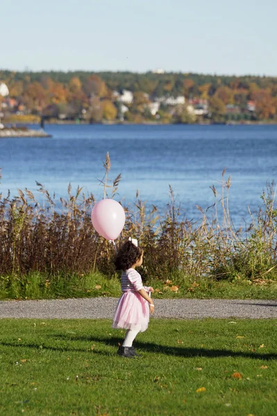 A girl holding a balloon next to the water