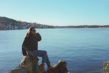 Göl kenarındaki ağaç gövdesinde oturan kadın berrak gökyüzüne karşı