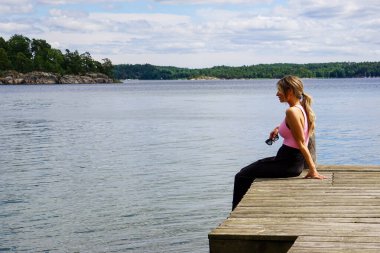 Gökyüzüne karşı iskelede oturan kadının yan görüntüsü