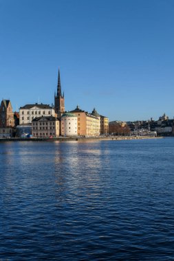 View of buildings by river against clear blue sky