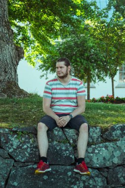 Parktaki taş duvarda oturan bir adam.