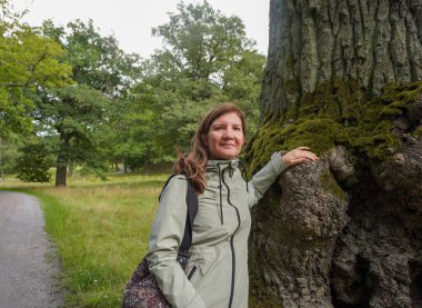 Ormanda ağaç gövdesine yaslanan gülümseyen kadın portresi