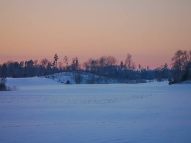 Gün batımında karla kaplı tarlalar gökyüzüne karşı