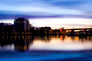 Gün batımında gökyüzüne karşı binaların nehir manzarası