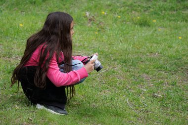 Tarlada çömelirken fotoğraf çeken bir kızın yan görüntüsü 