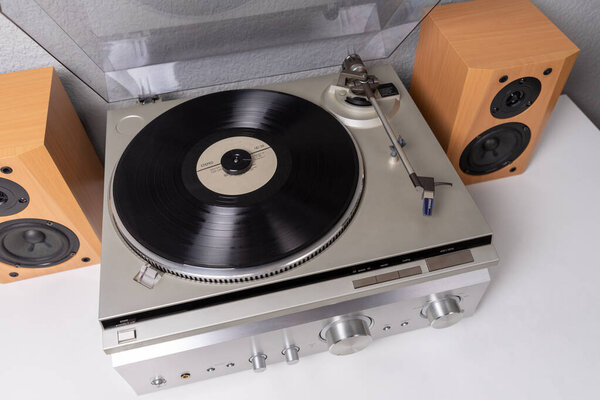 vintage vinyl player with amplifier and loudspeakers on white table