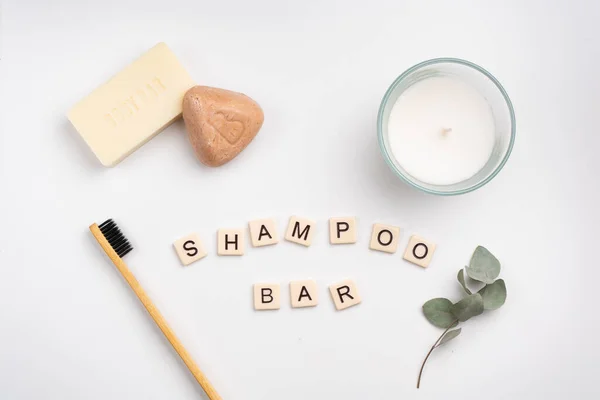Flat lay of body and shampoo bars, bamboo toothbrush, candle on white background.  SHAMPOO BAR written with tile letters