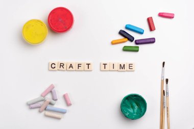 Flat lay of colorful creative supplies. Paints, crayons, chalk and paintbrushes on white background. CRAFT TIME written with tile letters  clipart