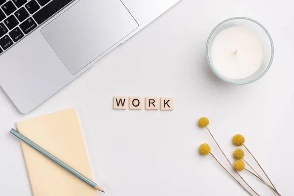 stock image Clean workspace with laptop, pencil and notebook, candle and flowers on white background. The word WORK written with tile letters. Flat lay