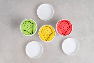 Gri arka planda beyaz kavanozlarda renkli hamurlar. Düz yatıyordu