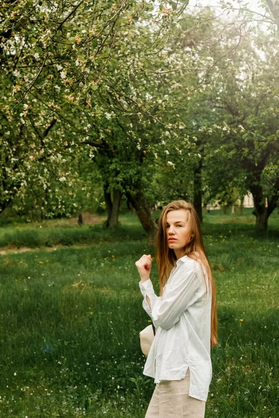 A beautiful young woman with long fair hair in light clothes in the fruit garden