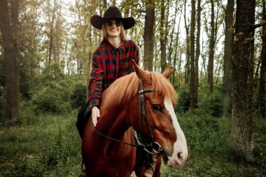 Genç ve güzel sarışın kadın, uzun saçlı, kestane rengi bir atın üstünde oturuyor.
