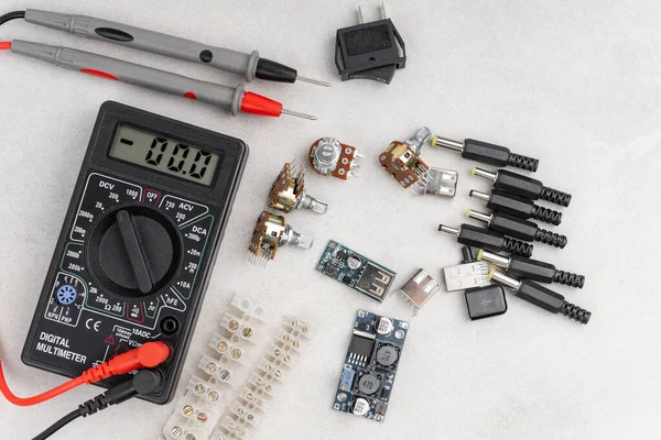 stock image arrangement of different electrical tools on grey background. multimeter, converter, adapters, heat shrink etc.