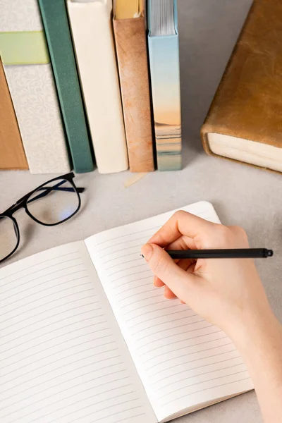 Siyah kalemi açık deftere yazmaya hazır bir el. Arka plandaki kitaplar..