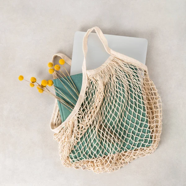 stock image green book and silver laptop with yellow flowers in beige string bag