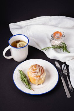 Beyaz seramik tabaklarda ev yapımı tarçınlı rulo biberiye ve bir fincan çayla süslenmiş.