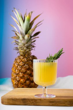 Bir bardak ananas suyu ve parlak pembe arka planda bir ananas.