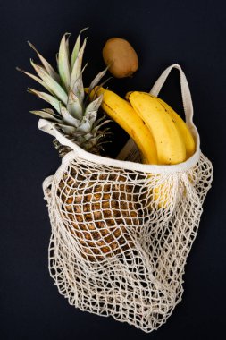 Muz, kivi ve ananas siyah arkaplanda bej bir sicim torbasında