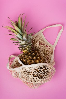 Pembe arka planda bej bir sicim torbasında ananas