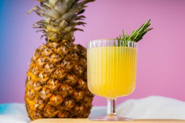 Bir bardak ananas suyu ve parlak pembe arka planda bir ananas.