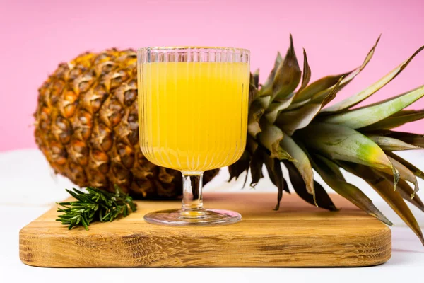 Bir bardak ananas suyu ve parlak pembe arka planda bir ananas.