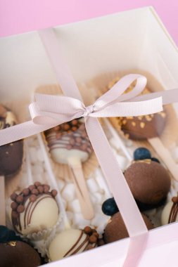 Çubuk şekerleme ve kremalı şekerlemeler pembe arka planda beyaz kutuda.