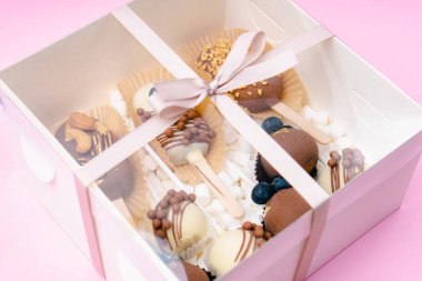 Çubuk şekerleme ve kremalı şekerlemeler pembe arka planda beyaz kutuda.