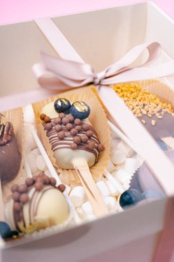 Çubuk şekerleme ve kremalı şekerlemeler pembe arka planda beyaz kutuda.