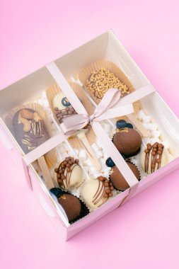 Çubuk şekerleme ve kremalı şekerlemeler pembe arka planda beyaz kutuda.