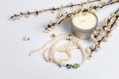 Bir dizi inci, bir mum ve beyaz arka planda açan dallar.