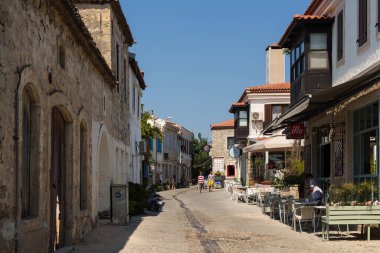 Ünlü, turistik Ege kasabası Alacati 'de eski, tarihi ve geleneksel taş evlerde yürüyen insanları görmek. Bu, Cesme ilinin bir köyüdür. Güneşli bir yaz günü.