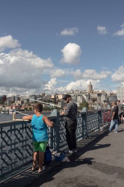 İstanbul 'daki Galata Köprüsü' ndeki balıkçıların görüntüsü. Arka planda Galata kulesi ve Beyoğlu bölgesi var. Görüntü, yerel halkın yaşam tarzını ve kültürünü yansıtıyor. Güneşli bir yaz günü..
