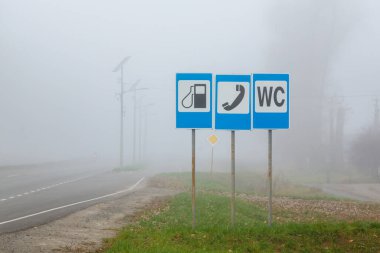 Yolun kenarında benzin istasyonu, telefon ve otoban tuvaleti olduğunu gösteren bir tabela var..