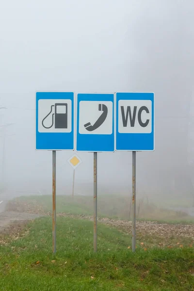 A road sign on the side of the road indicating that there is a petrol station, telephone and freeway toilet nearby.
