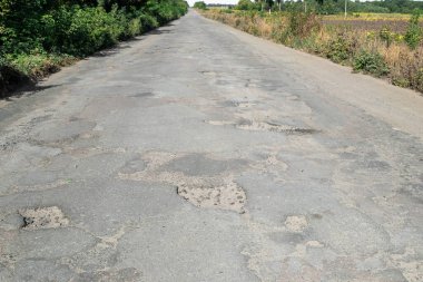 Kötü yol, asfalt çatlamış çukurlar ve büyük delikler. Yoldaki çukurlar ve asfaltta taşlar. Asfalt yüzeyi yolda yok oldu. Yolun kötü durumda, onarılması gerekiyor..